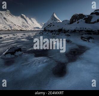 Interessanti texture ghiacciate in primo piano dell'iconica montagna Volandstind vicino a Fredvang a Lofoten, Norvegia, durante una fredda giornata di sole invernale. Foto Stock