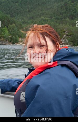 Una donna sorridente seduta su una piccola barca che indossa un giacca impermeabile e giubbotto salvagente / salvagente Foto Stock