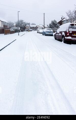 Una strada residenziale a Reading, Berkshire, Regno Unito è coperta di neve. Le piste dell'auto conducono in lontananza. Foto Stock