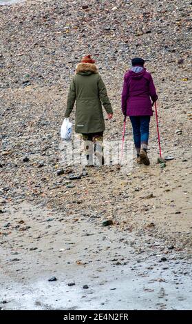 Due donne che camminano sul Tamigi sul lungofiume utilizzando bastoni per nordic walking. Sono impallidenti alla ricerca di manufatti storici. Londra. Foto Stock