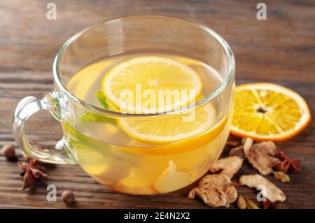 Bicchiere di tè caldo allo zenzero con limone, spezie e menta piperita su sfondo di legno. Concetto di bevande calde alle erbe invernali Foto Stock