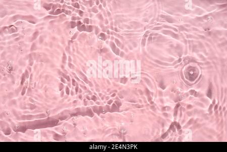 Consistenza d'acqua rosa con increspature, onde e bolle. Primo piano di riflessi solari e ombre su una superficie d'acqua testurizzata. Retrogrun estivo astratto alla moda Foto Stock