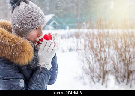 donna di mezza età che tiene una tazza di bevanda calda e sorridente sullo sfondo di una strada invernale. sparare all'aperto. Foto Stock