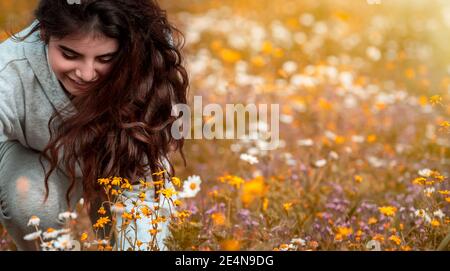 Ritratto di una ragazza carina con gioia che raccoglie fiori selvatici in bouquet. Trascorrere le vacanze primaverili in campagna. Godetevi la fresca natura di Springtime. Foto Stock