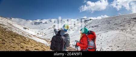 Vista posteriore su due allegri Sportsman Passeggiate nelle Snowy Mountains con Trekking Poles. Scegliere il modo giusto. Vacanze invernali attive. Foto Stock