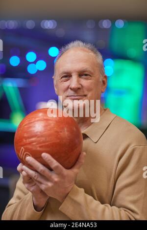 Verticale vita in su ritratto di sorridente anziano che tiene il bowling palla e guardare la fotocamera mentre ti godi l'intrattenimento attivo a. pista da bowling Foto Stock