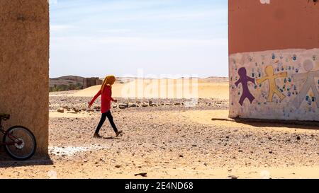 La ragazza marocchina corre tra due edifici scolastici nel Sahara deserto in estate Foto Stock