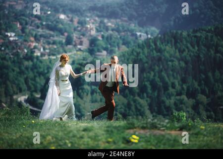 felice elegante sposa e sposo correre e divertirsi in montagna in estate soleggiato giorno. bella coppia newlywed ridere, veri sentimenti. emotivo rom Foto Stock