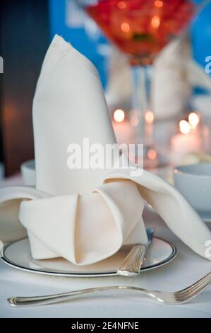 Tovagliolo bianco piegato su piatti raffinati con bicchiere cocktail E candele in background Foto Stock