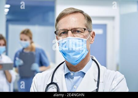 Medico anziano maturo che indossa la maschera facciale guardando la macchina fotografica. Foto Stock