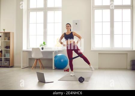 Giovane atleta allegra in abbigliamento sportivo che fa esercizio con fitness gengive online Foto Stock