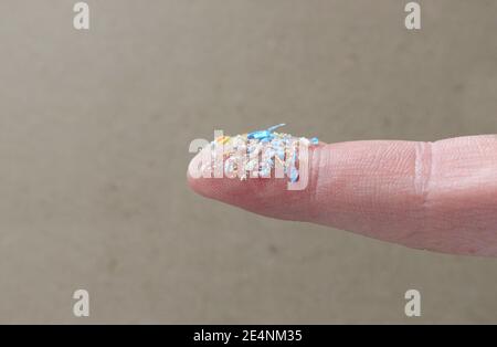 Primo piano della foto laterale delle microplastiche su un dito umano. Concetto creativo di inquinamento idrico e riscaldamento globale. Idea del cambiamento climatico. Un mazzo di plastica Foto Stock