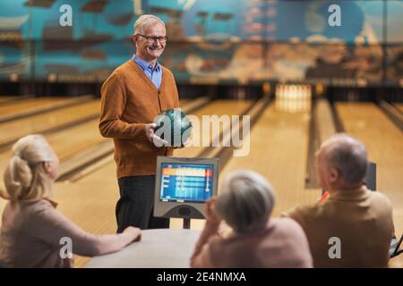 Ritratto di felice anziano sorridente a gruppo di amici mentre si gioca a bowling insieme al centro di intrattenimento, copia spazio Foto Stock