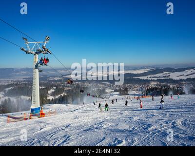 Piste da sci, seggiovia, sciatori e snowboarder nella località sciistica di Bialka Tatrzanska in Polonia in inverno. Cannoni da neve in azione Foto Stock