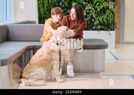 Madre e figlio seduti sul divano con il loro cane e in attesa di visita al veterinario in clinica Foto Stock