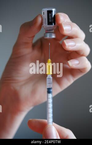 Flaconcino di vaccino originale Pfizer-BioNTech COVID-19 tenere in mano con l'ago della siringa accanto. Foto di vaccino reale. Messa a fuoco selettiva. Stafford, Regno Unito Foto Stock