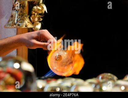 Artigiano che lavora un oggetto decorativo natalizio in vetro, che lo gira sotto la sua torcia, al mercatino di Natale di Bressanone, Alto Adige, Italia Foto Stock