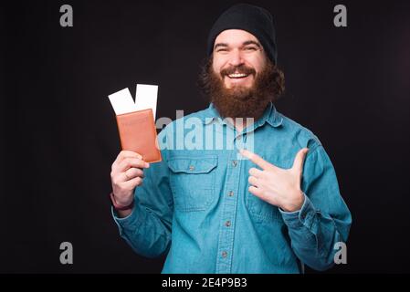 Foto di un hipster sorridente che indica il passaporto e i biglietti. Foto Stock