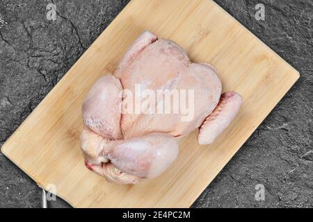 Pollo intero crudo su tagliere di legno Foto Stock