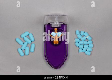 una taglierina per pillola viola e arancione con una pillola blu tagliare a metà sotto la lama e un mucchio di pillole intere su un lato e un mucchio di taglio pillole sul othe Foto Stock