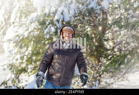 un uomo con barba e baffi, con cappello e giacca in pelliccia, in una giornata di sole in una foresta invernale Foto Stock