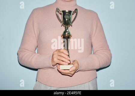 Un'immagine ritagliata di una donna matura irriconoscibile che tiene il trofeo mentre si sta in piedi su sfondo blu, spazio di copia Foto Stock