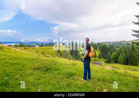 Un ragazzo viaggia con uno zaino giallo attraverso luoghi pittoreschi con splendidi paesaggi di montagna. Foto Stock