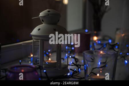 Primo piano di candele di tè in lanterna e bicchieri sulla soglia. Luce blu. Higge decorazioni natalizie. Foto Stock