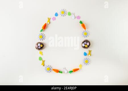 Pasqua creativa. Posa piatta con forma dell'uovo, cornice di uova caramelle e un altro arredamento festivo. Carote decorative, conigli, polli, fiori sulla risata Foto Stock