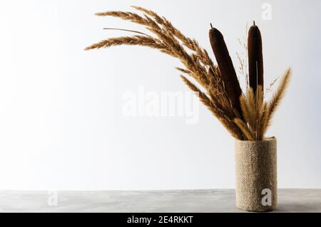 Un bouquet autunnale di pikelet e semi in un vaso coperto con un panno grossolano su un ripiano contro una parete bianca. Messa a fuoco selettiva. Foto Stock