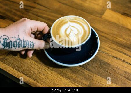 GRAN BRETAGNA / Inghilterra / Londra / mano con tatoo che tiene il caffè Cup in un caffè al coperto a Londra.Close up di mani per tenere una tazza di caffè Foto Stock