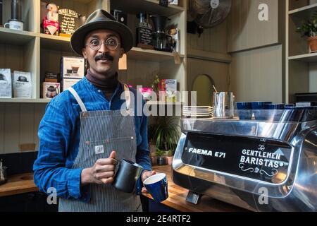 barista con grembiule che versa il latte in cottura a vapore in una tazza di caffè, per la preparazione di latte art Foto Stock