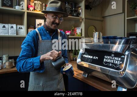 barista con grembiule che versa il latte in cottura a vapore in una tazza di caffè, per la preparazione di latte art Foto Stock