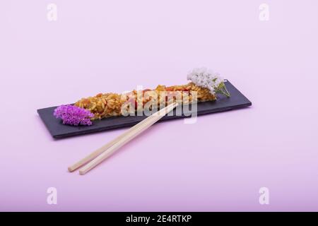 Un piatto di riso fritto decorato con fiori su un sfondo rosa Foto Stock