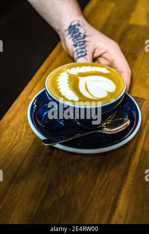 GRAN BRETAGNA / Inghilterra / Londra / mano con tatoo che tiene il caffè Cup in un caffè al coperto a Londra.Close up di mani per tenere una tazza di caffè Foto Stock