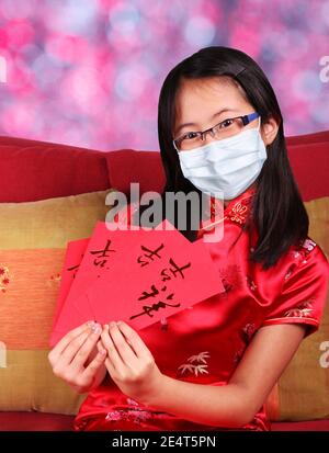 Festeggiando il nuovo anno cinese durante la pandemia di Covid-19 con la ragazza felice indossare maschera e cheongsam tradizionale qipao con buste soldi rossi Con CH Foto Stock