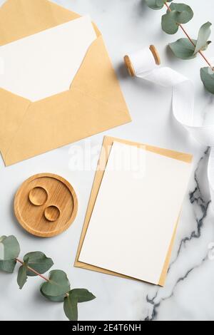 Eleganti inviti per matrimoni, buste di carta artigianali, anelli, rami di eucalipto su scrivania in marmo. Set di cancelleria rustica per matrimoni. Disposizione piatta, vista dall'alto. Foto Stock