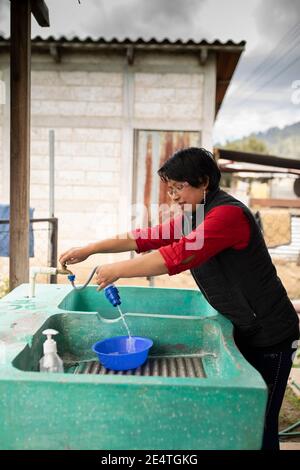 Una donna utilizza un sistema di filtrazione dell'acqua pulita basato sul rubinetto a casa sua a Cantel, Guatemala. Foto Stock