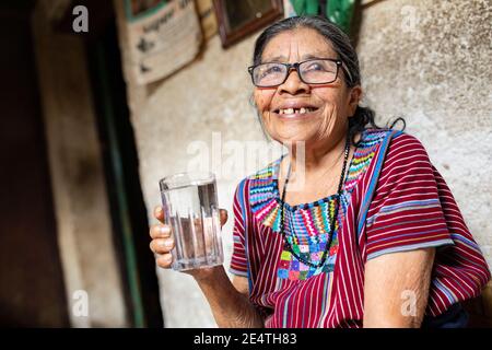 Una donna anziana beve un bicchiere d'acqua pulita a San Juan la Laguna, Guatemala, America Centrale. Foto Stock