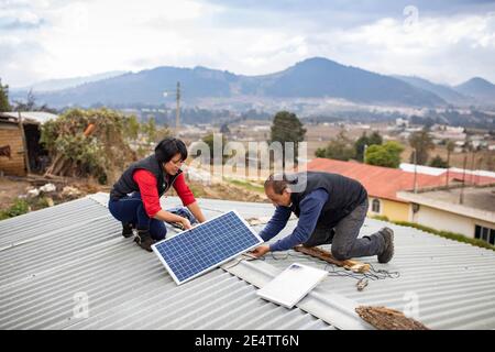 I tecnici della società locale di energia senza scopo di lucro installano un nuovo sistema di illuminazione a energia solare in una casa a Cantel, Guatemala, CEN Foto Stock