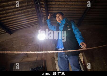 Un tecnico della società locale di energia senza scopo di lucro prova un nuovo sistema di illuminazione a energia solare in una casa a Cantel, Guatemala, America Centrale. Foto Stock