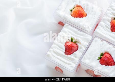 Shortcake di fragole in scatola di plastica su con fondo di stoffa e spazio di copia, il concetto minimo di torta e panificio Foto Stock