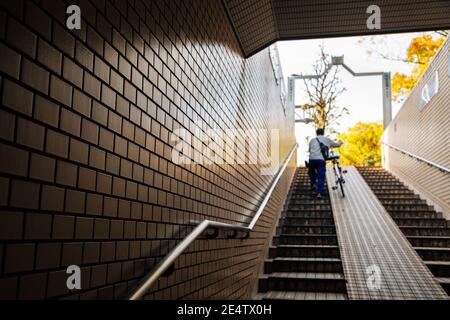 Uomo che sale scale con bicicletta in Giappone Foto Stock