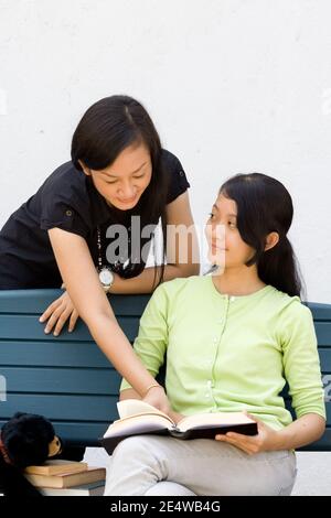 Ritratto di due ragazze del sud-est asiatico, una in piedi e una seduta su una panchina, discutendo su un libro Foto Stock