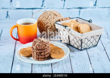 Biscotti assortiti in piatto e cestino e una tazza sopra tabella blu Foto Stock