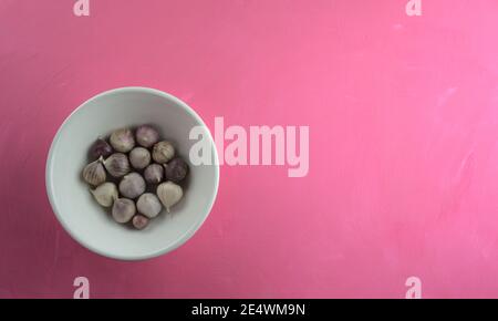 Aglio in ciotola su fondo di tela rosa acrilico graffiato. Cibo, cucina, mangiare, fotografia di natura morta con spazio di copia. Foto Stock