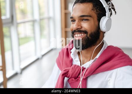Allegro ragazzo afroamericano sorridendo e ascoltando musica con le cuffie in ufficio Foto Stock