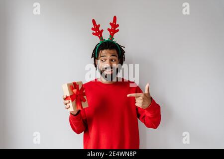 Divertente uomo afroamericano in presa e puntando il dito a. confezione regalo isolata su sfondo bianco Foto Stock