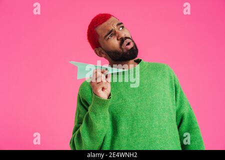 Sorprende l'afro americano ragazzo che tiene l'aereo di carta isolato sopra il rosa sfondo Foto Stock