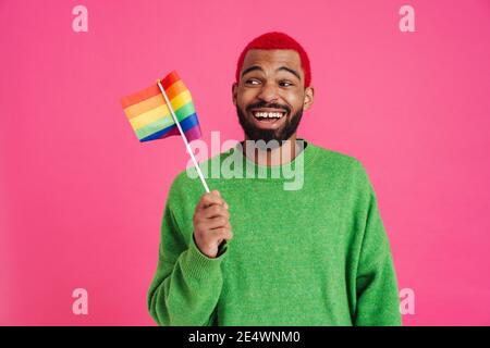 Gioioso ragazzo afroamericano ridendo e tenendo la bandiera arcobaleno isolato su sfondo rosa Foto Stock
